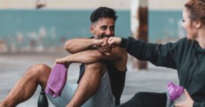 Man and woman sitting on gym floor post-workout fist bumping.