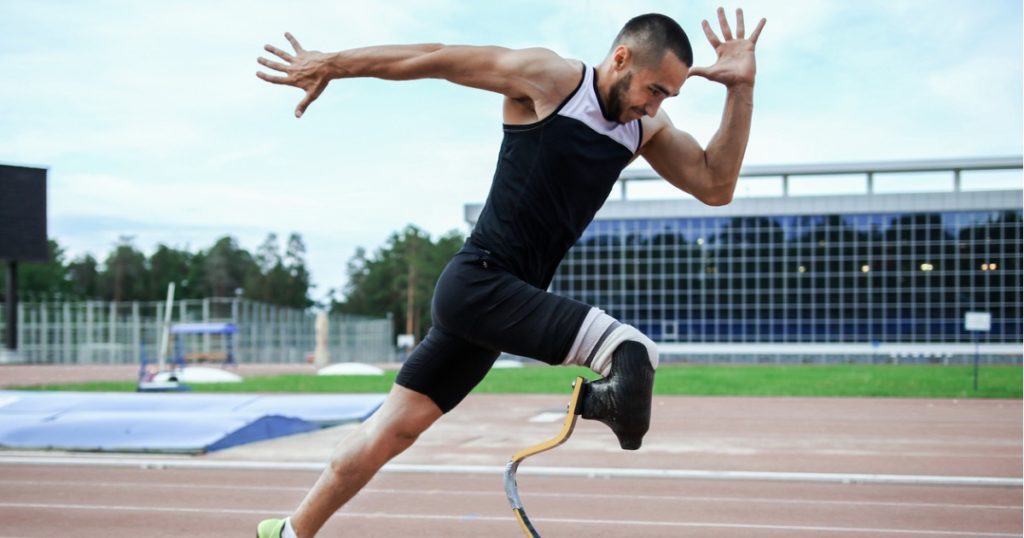 Male athlete with a prosthetic leg in an explosive running position on an outdoor running track.