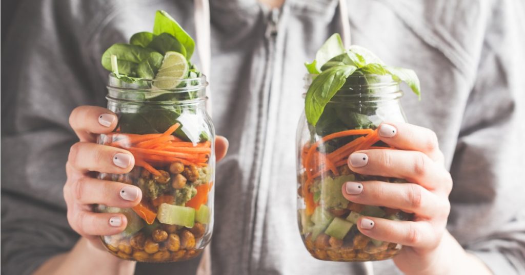 Closeup of hands holding chickpea salads in a glass jar.