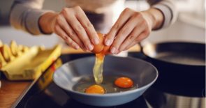 Closeup of hands cracking an egg into a pan on the stove.